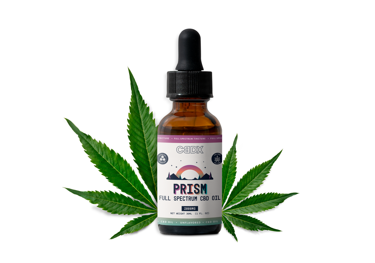 A bottle of CBDX Prism Full Spectrum Hemp Oil centered on a white background, flanked by two green cannabis leaves.